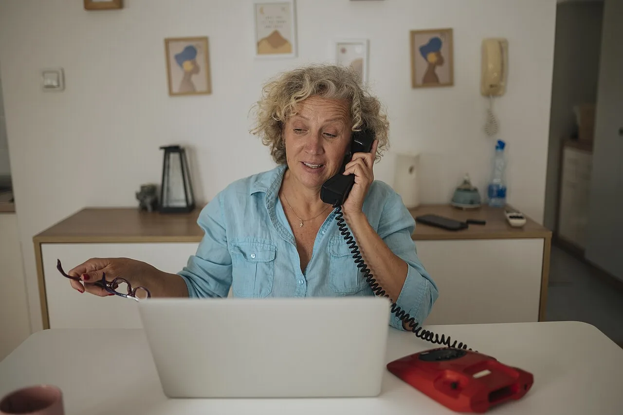 Adult woman using a laptop while speaking on a telephone at home